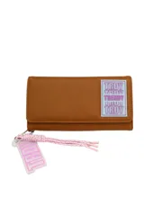 Billetera marrón con cierre de solapa y botón a presión. Tiene un aplique rectangular con el logo de la marca en celeste y blanco. Incluye un llavero con cordón trenzado rosa y blanco y un dije con el logo de la marca.