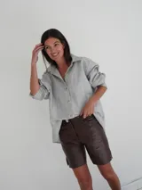 Bermuda de cuero color marrón, con corte recto, bolsillos laterales y cierre frontal con botón dorado.