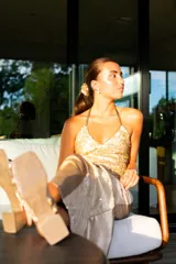 Top de lentejuelas doradas con escote en V y diseño halter. Presenta un ajuste al cuello y espalda descubierta con tiras cruzadas.