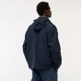 Chaqueta cortavientos azul marino con capucha, cierre frontal y bolsillos con solapa a la altura de la cintura. Presenta un diseño técnico y holgado.