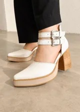 Zapatos de tacón alto color blanco con plataforma y doble correa con hebillas en el tobillo. Cuenta con taco ancho de madera y diseño en punta fina.