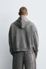 Sudadera con capucha y cierre de cremallera, de corte relajado (relaxed fit), confeccionada en algodón con interior afelpado. Presenta bolsillos frontales tipo canguro y acabados en rib. El tejido tiene un efecto lavado que le da un color negro desgastado.