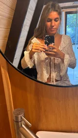 Blusa blanca de encaje con cuello en V, mangas largas acampanadas y lazo ajustable en el frente.