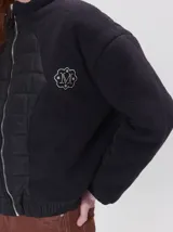 Campera crop de corte boxy y color negro, forrada en corderito, con parches capitoneados en el pecho y las mangas. Cuenta con cierre frontal metálico, cuello alto, puños y bajo elastizados, y detalle de logo bordado en hilo en el pecho.