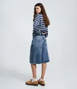 Bermuda tipo jorts de jean azul con lavado medio, corte holgado y largo por debajo de la rodilla. Presenta cintura con trabillas, bolsillos laterales y traseros, y cierre frontal con botón y cremallera.