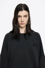 Buzo de algodón color negro con efecto gastado, corte globo y mangas largas ranglán. Presenta un logo bordado discreto en el pecho.