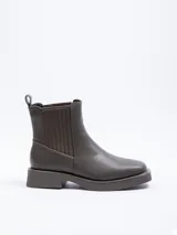 Bota corta tipo chelsea de cuero sintético color verde oliva, con plataforma y punta cuadrada. Presenta paneles elásticos laterales acanalados y tirador en la parte trasera.