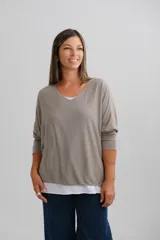 Sweater de punto color beige con diseño de doble capa, escote en V con detalle de vivo plateado y mangas largas. Presenta un corte amplio y holgado.