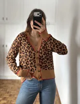 Saco de punto con estampado animal print, cuello en V y cierre frontal con botones. Presenta detalles de ribetes en color rojo en el cuello, puños y ruedo.
