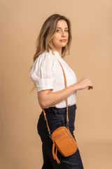 Bandolera compacta color rosado, con correa regulable y desmontable. Tiene apertura superior, bolsillo frontal con cierre y detalle de borla, y bolsillo trasero sin cierre. El interior está forrado en tela y cuenta con un bolsillo adicional.