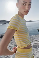 Top corto de punto con diseño a rayas horizontales en color amarillo y blanco, cuello redondo y manga corta.