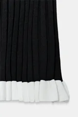 Vestido corto de punto canalé negro, con cuello barco, sin mangas y detalle de volados blancos en el borde inferior.