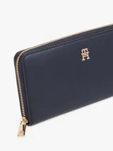 Billetera rectangular de color azul marino con acabado liso y cierre perimetral de cremallera dorada. Presenta una insignia metálica con el monograma TH en el frente.