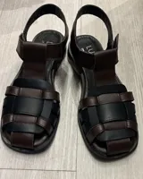 Sandalias tipo guillermina de cuero vacuno color negro, con diseño de tiras entrelazadas, punta cuadrada y tira ajustable en el talón.