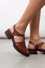 Sandalias de cuero color negro, tipo cangrejera, con diseño de tiras entrelazadas, tira en T, hebilla de ajuste en el tobillo, suela track y tacón cuadrado de madera.