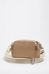 Bolso tipo morral Bimba y Lola, de color tostado, confeccionado en nylon suave con detalles en cuero y tirantes de cordón. Cuenta con múltiples compartimentos con cierre y el logo metálico de la marca en el frente.