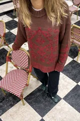 Buzo de tejido de punto grueso color marrón con diseño geométrico y floral estampado en color rojo. Presenta cuello redondo, mangas largas y puños y ruedo acanalados.
