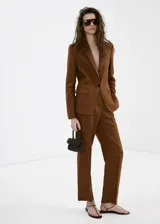 Blazer de lino color marrón, de diseño recto, con cuello pico con solapa, manga larga y cierre de un botón en la parte delantera.