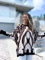 Sweater de punto con diseño oversize y estampado abstracto en tonos negro, beige y blanco. Presenta cuello redondo, mangas largas con puños ajustados y un corte holgado que cae suavemente sobre la figura.