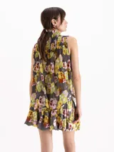 Top sin mangas confeccionado en crepé estampado con diseño floral en tonos amarillos, rosas y verdes sobre base gris. Cuenta con cuello alto fruncido y detalles de nido de abeja en el canesú.