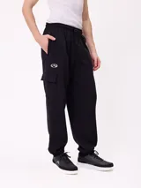 Babucha de estilo cargo en color negro, confeccionada en tejido de algodón y poliéster. Presenta cintura elástica con cordón ajustable, bolsillos laterales tipo cargo y puños elásticos en los tobillos.