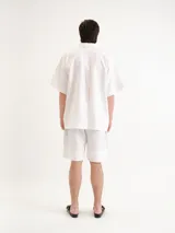 Camisa blanca de manga corta, con cuello clásico, cierre frontal con botones y un bolsillo aplicado en el pecho.