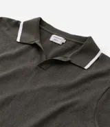 Camisa polo de manga corta color verde oliva, confeccionada en tejido de punto, con cuello y puños con ribetes contrastantes en blanco y rojo.