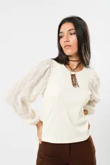 Blusa color manteca de cuello redondo y mangas largas abullonadas con puños elásticos.