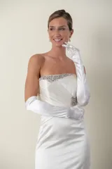 Vestido de novia largo color marfil, confeccionado en piel de ángel drapeada. Diseño strapless con apliques bordados en piedras en el escote, la cintura y la cola. Incluye guantes largos de satén blanco.