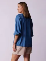Blusa celeste de tencel con cuello redondo, escote en V y lazo de ajuste. Tiene cuello y escote calado y mangas 3/4 amplias con puño elastizado.