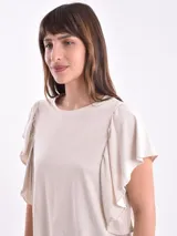 Remera blanca de algodón con cuello redondo y mangas cortas con volados fruncidos en los hombros.