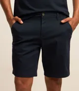Bermuda masculina slim confeccionada en sarga de algodón con elastano, color beige, con bolsillos laterales tipo chino, bolsillos traseros embutidos con botón, trabillas en la cintura y cierre frontal con botón y cremallera.