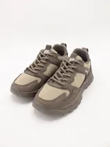 Zapatillas urbanas de estilo trekking, color taupe (marrón claro/beige), con suela gruesa y detalles superpuestos en material sintético y textil.