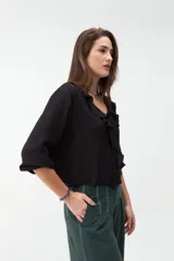 Blusa negra de manga larga con cuello en V adornado con volados frontales y lazos ajustables.