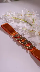 Cinturón naranja con aplique de cadena dorada.