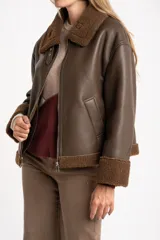 Campera tipo gamulán de cuero sintético marrón con interior y detalles de corderito en cuello, puños y ruedo. Presenta cierre frontal metálico y corte oversize.