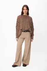 Sweater de punto con diseño de trenzas verticales, cuello redondo y corte crop. Presenta una combinación de colores crudo y camel, con mangas largas y ajuste holgado.