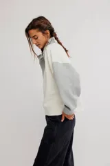 Buzo de frisa con diseño colorblock en tonos blanco y gris, cuello alto con botones a presión frontales, mangas largas raglán y puños y cintura acanalados.