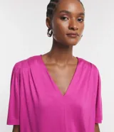 Blusa fucsia de viscolycra crepada, con escote en V y mangas cortas con detalle de pliegues en los hombros.