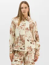 Conjunto de dos piezas compuesto por camisa de manga larga con cuello solapa y botones frontales, y pantalón de tiro alto con pierna recta y bolsillos laterales. Ambas prendas presentan un estampado paisajístico en tonos marrones sobre fondo crema.