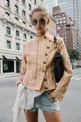 Cazadora de jacquard con estampado de rayas y detalles florales en tonos rosados y beige, cuello redondo, manga larga, bolsillos delanteros de vivo y cierre frontal cruzado con botones metálicos.