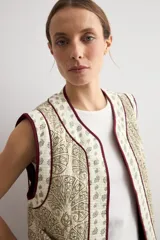 Chaleco capitoneado sin mangas, de color blanco con estampado paisley en tonos beige y verde, con ribetes en color bordó.