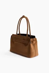 Bolso tote de acabado suave, color marrón, con asas tubulares unidas por una trabilla con hebilla metálica. Presenta una correa decorativa frontal con hebilla metálica y compartimento interior con cierre.