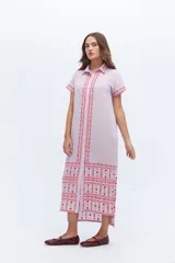 Vestido camisero de lino color lila con bordados rojos en contraste. Presenta un diseño de largo midi con cuello camisero, cierre frontal de botones y mangas cortas. Los detalles bordados recorren la botonadura, los puños y el ruedo de la prenda.