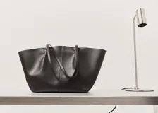 Bolso tipo shopper efecto piel de color marrón oscuro, con dos asas de hombro, detalles metálicos, cierre de botón magnético y forro interior.