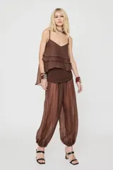 Pantalón marrón de corte ancho y estilo balloon, confeccionado en tejido translúcido con textura sutil y puños fruncidos en los tobillos.