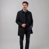 Gabardina impermeable negra con cierre frontal de botones, cuello clásico y ajuste en las mangas. Presenta un diseño minimalista con interior forrado a cuadros y múltiples bolsillos internos.