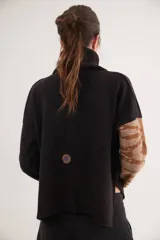 Polera de calce relajado con cuello alto, confeccionada en lana. Presenta un diseño bicolor con cuerpo en gris claro y mangas con estampado jacquard de arabescos en tonos tierra y negro. Incluye detalle de costura central vertical en el frente.