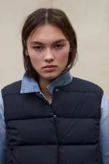 Chaleco acolchado blanco sin mangas, con diseño de franjas horizontales, cuello alto y cierre frontal con botones a presión. Modelo Olimpo de Ecoalf.