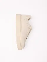 Championes de plataforma baja de color beige, con cordones tono sobre tono y detalle de placa metálica en los cordones.